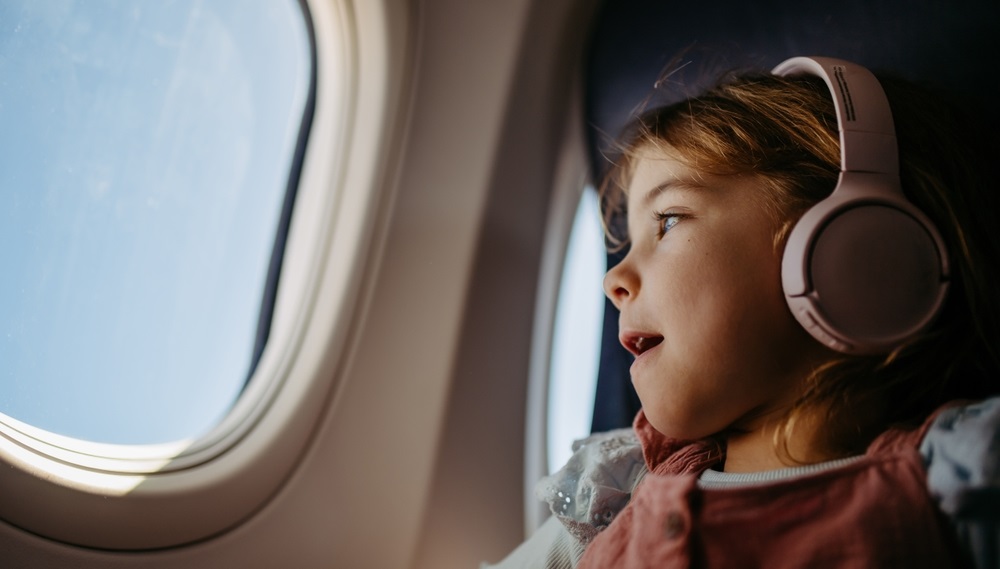 Photograph of a child looking out the window on an airplane with headphones on.